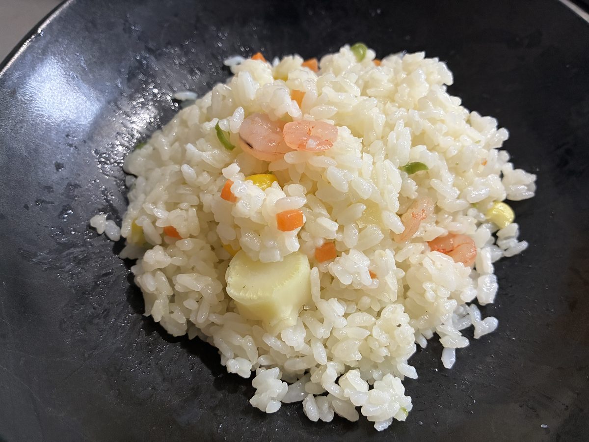 レンジで温めたえびピラフを黒い皿に盛ったところ。米粒はパラパラで、にんじん・いんげん・とうもろこしとえびが見える