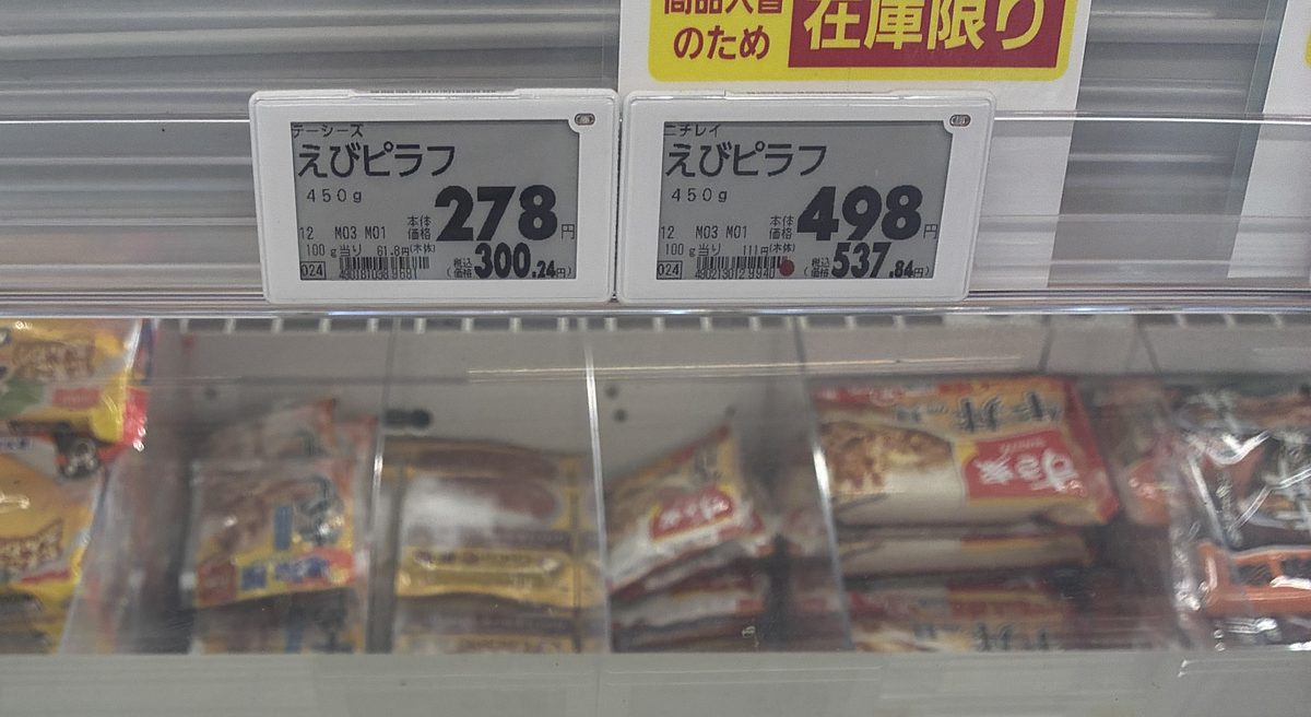 スーパーの冷凍ケースに並ぶ2つの値札。ターシーズのえびピラフ450gが本体278円、ニチレイのえびピラフ450gが本体498円と表示されている